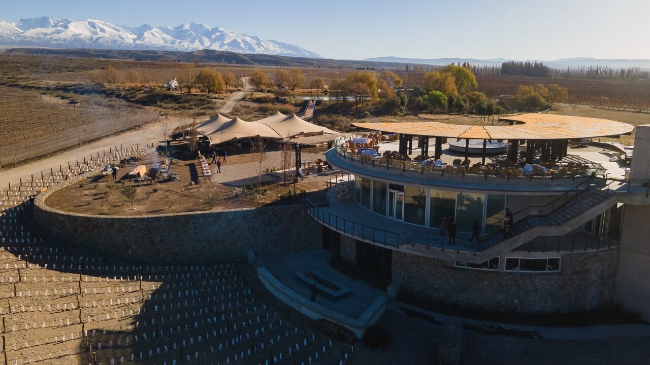 Aerial view of the winery complex: circular building, a marquee set up on the lawn, vineyard rows and the Andes beyond