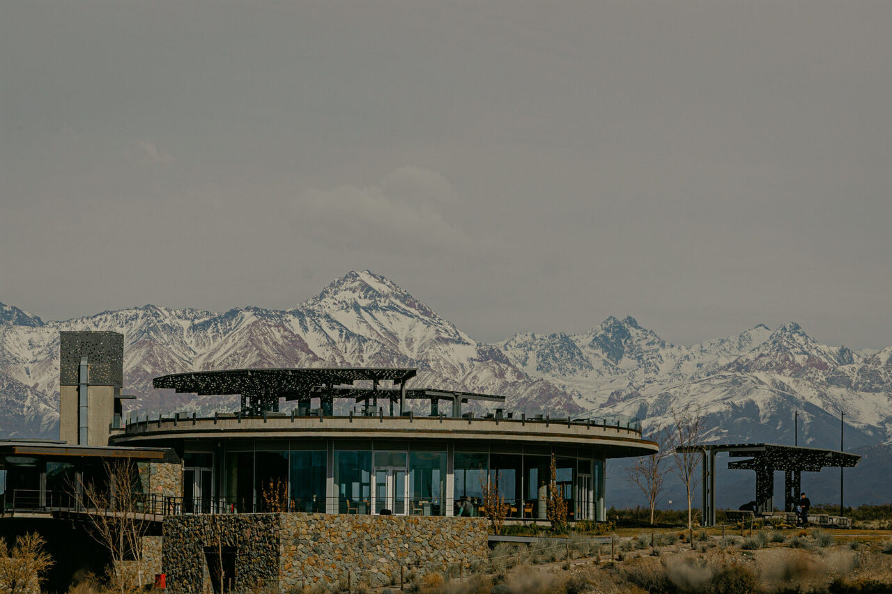 A circular stone-and-glass winery in Gualtallary, Mendoza, with the snow-capped Andes rising behind it
