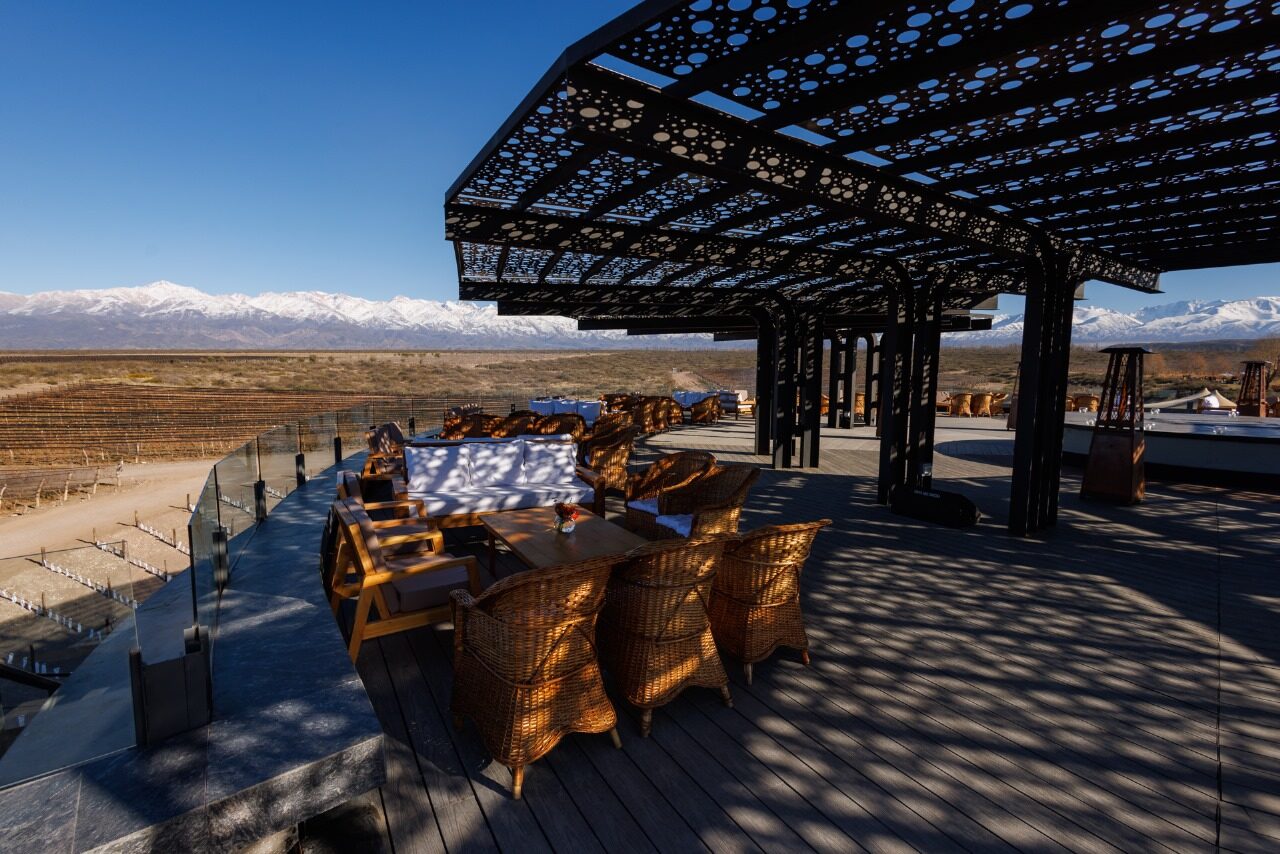 A long table laid under an openwork iron pergola on the winery terrace, with glassware and candles, the snow-capped Andes behind