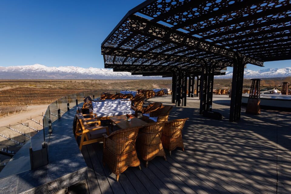 A long table set under a wrought-iron pergola on the winery terrace, with the Andes in the background