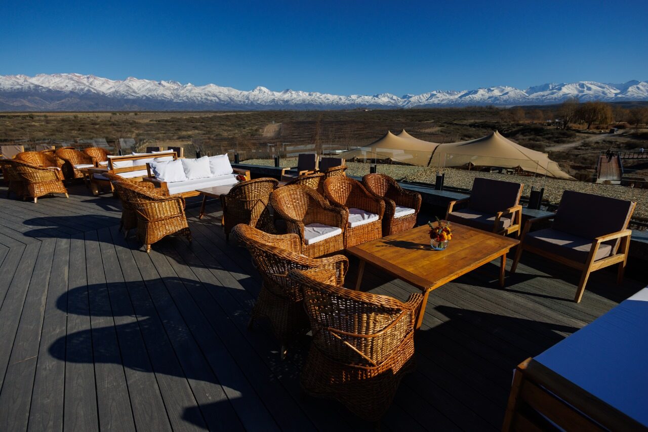 Wooden terrace with wicker armchairs facing the snow-capped Andes under a deep blue sky